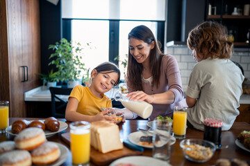 Children having breakfast with mother in home atmosphere. Cheerful little girl preparing cereals with mother.