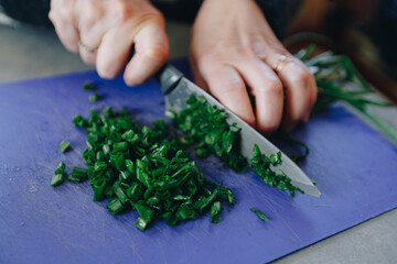 woman's hands chopping green onion on blue plastic cutting board