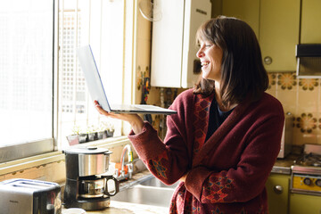 Adult Happy Woman smiling at home in a video call with her laptop in the kitchen