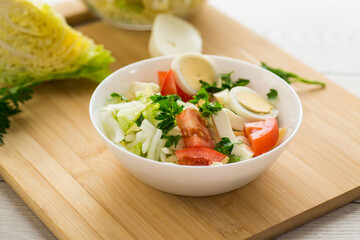 fresh vegetable salad, cabbage, tomatoes in a bowl on a wooden table
