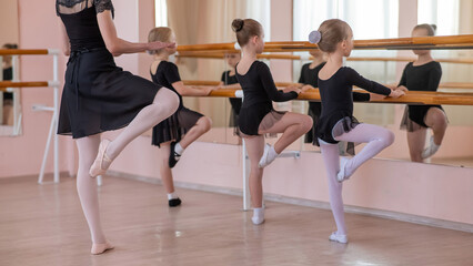 Caucasian woman teaches little girls ballet at the barre.