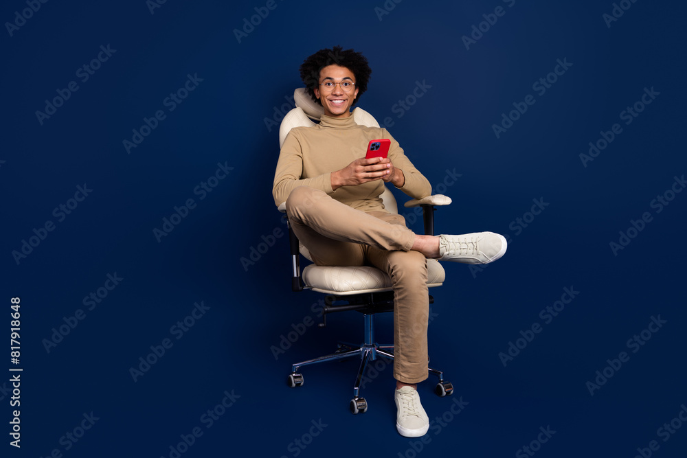 Poster Full size photo of nice young man sit armchair hold device wear trendy beige outfit isolated on dark blue color background