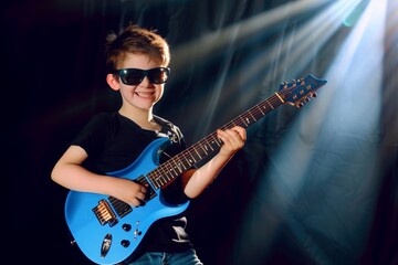 Obraz premium A young boy wearing sunglasses playing an electric guitar under dramatic stage lighting, smiling confidently.
