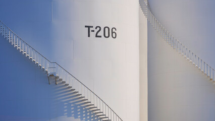 Spiral staircases on 2 white storage fuel tanks with sunlight and shadow on surface, oil industry...