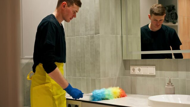 In an apartment cleaner cleans the surface of the bathroom sink with a dust brush