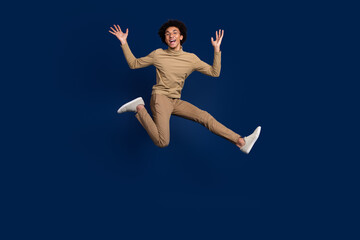 Full body photo of attractive young man jump running excited dressed stylish beige clothes isolated on dark blue color background