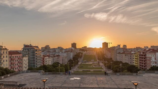Panorama showing sunset over lawn at Alameda Dom Afonso Henriques with colorful buildings and the Luminous Fountain aerial timelapse. View from above with evening sky in Lisbon, Portugal
