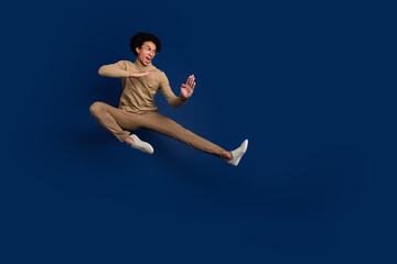 Obraz premium Full body photo of attractive young man fly kick karate dressed stylish beige clothes isolated on dark blue color background