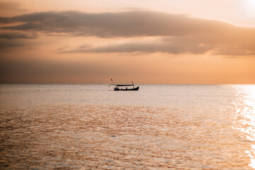 A fishing boat in the middle of the sea with a sunset background