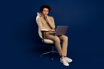 Full size photo of nice young man sit armchair netbook minded wear trendy beige outfit isolated on...