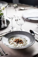 Halusky as traditional Slovak potato gnocchi with sheep cheese bryndza, fried bacon and chives served in a modern plate and on a festively laid restaurant table.