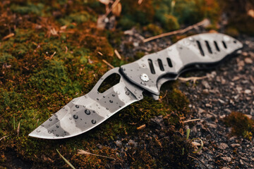 Tactical folding knife with water drops for survival on moss background