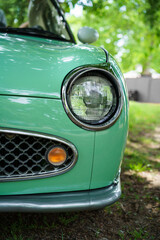 A green vintage car is parked from a front view in the shade of the trees. Oldtimer car. Classic...