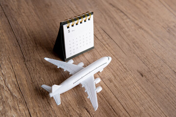 Toy airplane on a wooden table next to a calendar. Copy space for text. Flight reschedule, checking...