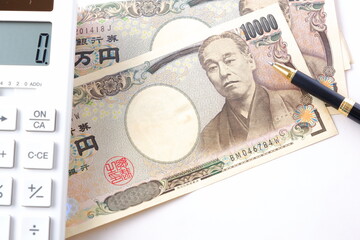福沢諭吉の肖像の一万円紙幣と電卓、ペン
