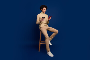Full body photo of attractive young man sit chair paper cup device dressed stylish beige clothes...