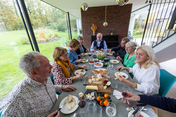 A vibrant scene of a group of elderly friends gathered around a dining table, enjoying a festive...