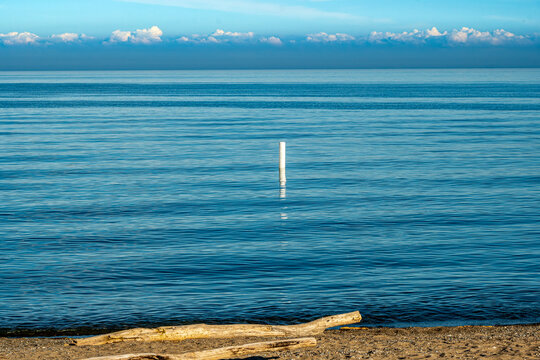 Calm evening on the beach with dift log in foreground blue smooth water with white safety bouy and clouds on the distant horizon shot kew beach toronto spring time room for text