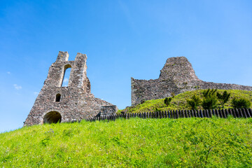 The ancient ruins of Potstejn Castle stand against a bright blue sky, surrounded by lush green...