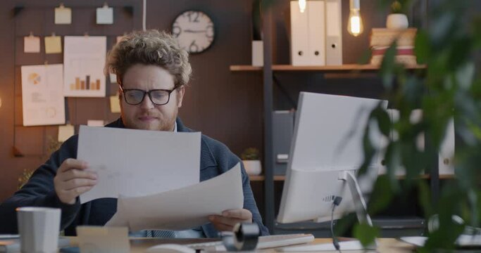 Loop of annoyed businessman reading documents then throwing papers away working in office in evening. Workload and paperwork concept.