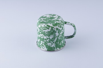 A typical Indonesian green and white iron cup on a white table with studio lighting