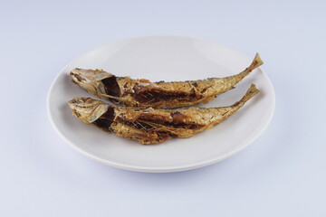 Fried mackerel on a white plate over a white background with studio lighting
