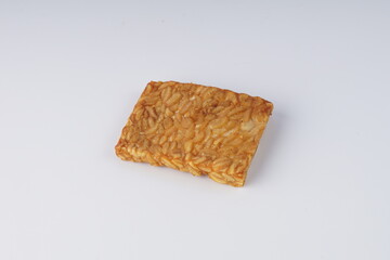 pieces of fried tempeh on a white plate on a white table with studio lighting