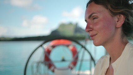 Tourist woman portrait enjoy cruise yacht trip to Bora Bora island, sailing at summer. Yacht ship helm rotates in background. Female relax outdoor lifestyle on sail yacht tropical travel vacation.