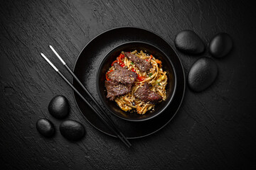Wok noodles udon with beef. Composition on black background. The Art of Japanese Cuisine. Food photography for menu and sushi bar decoration