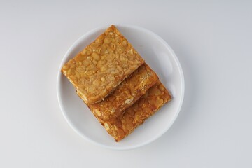 pieces of fried tempeh on a white plate on a white table with studio lighting