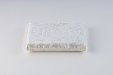 raw tempeh in plastic wrap on a white background with studio lighting