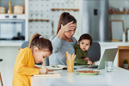 A stressed single mother working from home on a laptop and looking after her children