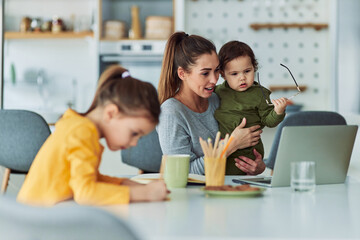 A dedicated single mother working from home using a laptop and watching over her two small kids