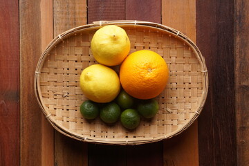 various types of oranges on a woven bamboo plate on a wooden background with studio lighting