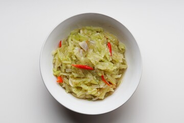 Stir-fried chayote vegetables with chopped garlic and red chilies in a white bowl on a white background
