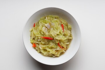Stir-fried chayote vegetables with chopped garlic and red chilies in a white bowl on a white...