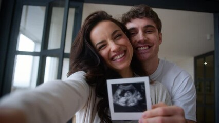 Caucasian family smiling happy laughing pregnant couple smile laugh woman pregnancy man female male guy girl hugging kissing cuddling showing demonstrate ultrasound image picture at home excited baby - Powered by Adobe