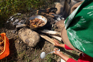 Obraz premium Indigenous woman cooking over firewood with metal pots and frying pan frying Cuy (guinea pig), traditional food of the Andes