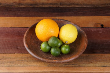 various types of oranges on a clay plate over a wooden background with studio lighting