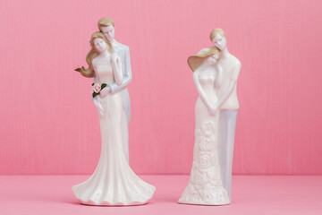 Two porcelain wedding figurines of couples embracing, set against a pink background with one couple holding a bouquet of flowers.