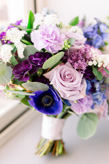 A gorgeous lavender rose and purple flowers bouquet sitting on a window ledge 