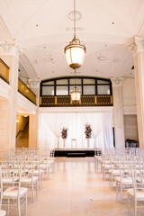 A beautiful ballroom space set up for a wedding ceremony with white chairs 