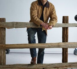 Cowboy leaning on wood split rail farm fence. 
