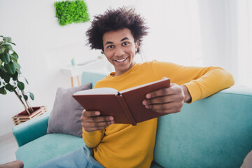 Portrait of nice young man hold read book wear yellow pullover white interior flat indoors