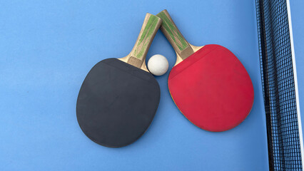 Two table tennis rackets and balls on a blue table with net.