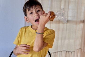 Latin boy looking at the camera eating dulce de leche from a sleeve while making typical...