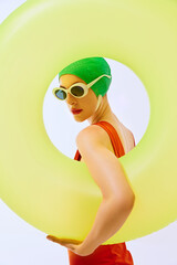 Elegant woman in green swim cap and white sunglasses, framed by large yellow inflatable ring,...