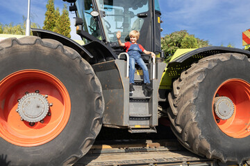 child sits happily on a huge farm tractor. Equipment for agriculture and agribusiness. The boy's...