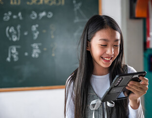 A girl is smiling while holding a cell phone in front of a blackboard with math equations on it....