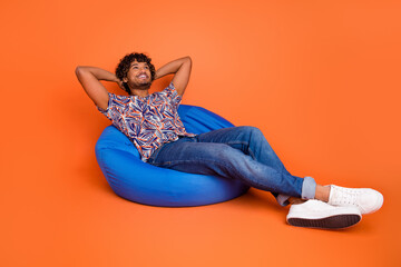 Full body photo of attractive young man bean bag hands behind head dressed stylish colorful clothes isolated on orange color background